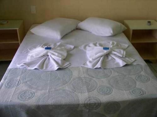 Una cama con toallas blancas encima. en Hotel Pousada Mineirinho, en Balneário Praia do Leste