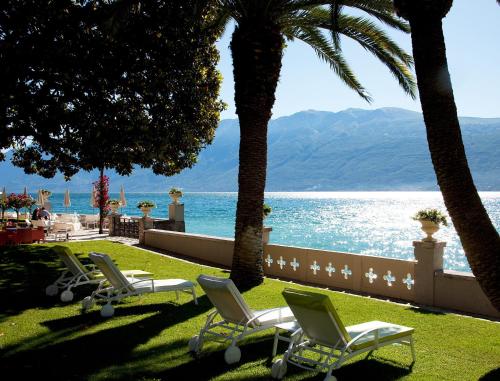 a row of lawn chairs and palm trees near the water at Hotel Villa Giulia in Gargnano