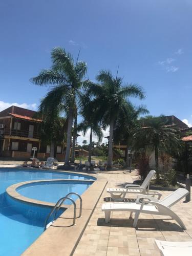 a pool with chairs and palm trees next to a building at Chalé Temporada Porto dos Lençóis - Lençóis Maranhenses in Barreirinhas
