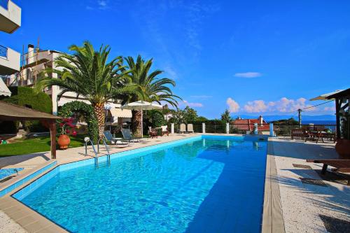une grande piscine avec de l'eau bleue et des palmiers dans l'établissement Coral Suite, à PalaiónTsiflíkion