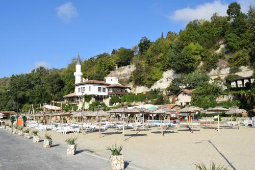 a beach with chairs and umbrellas and a mosque at Ahilea Hotel - Free Pool Access in Balchik