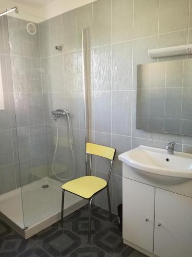 La salle de bains est pourvue d'un lavabo, d'une douche et d'une chaise jaune. dans l'établissement Villa bord de mer Corse, à Santa-Maria-Poggio