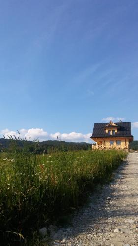 a house in a field next to a dirt road at Góralskie Domki na Podhalu - z jacuzzi in Maniowy