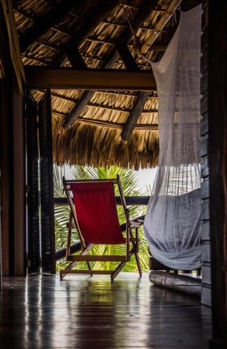 a red chair sitting on a porch with a thatch roof at El Alquimista Yoga Spa in Zipolite