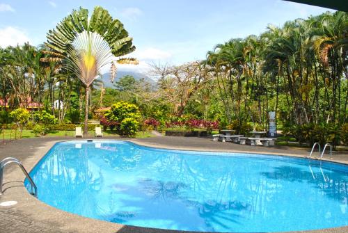 a blue swimming pool with a palm tree in the background at Hotel Arenal Country Inn in Fortuna