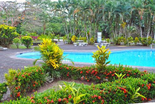 a swimming pool with plants and flowers in a park at Hotel Arenal Country Inn in Fortuna