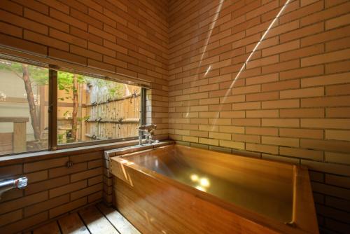 a bath tub in a brick walled room with a window at Shouhakutei Azumaso in Tendo