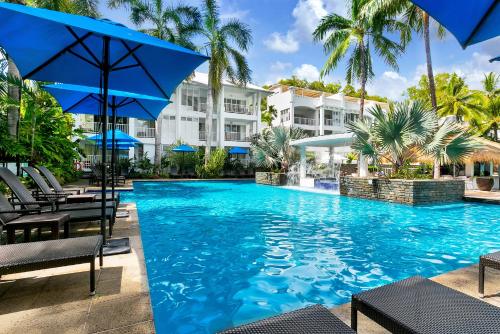a swimming pool with chairs and an umbrella at Beach Club Private Apartments Palm Cove in Palm Cove