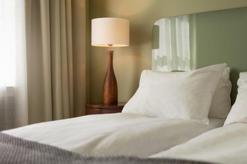 a bed with white sheets and a lamp on a table at Grand Hotel Terminus in Bergen