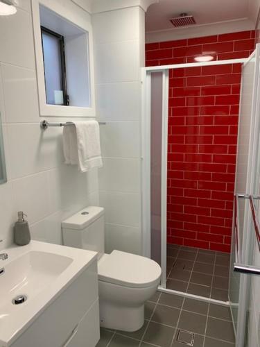 a bathroom with a white toilet and a red brick wall at Huskisson Beach Escape in Huskisson