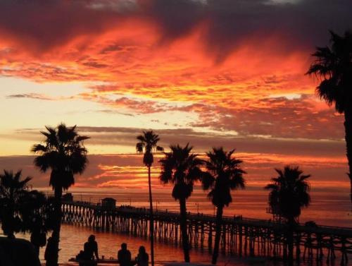 a sunset over the beach with palm trees and a pier at Sea Horse Resort in San Clemente