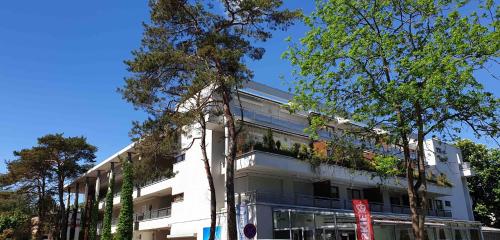 um edifício branco com árvores em frente em Apartament Jurata Deluxe em Jurata