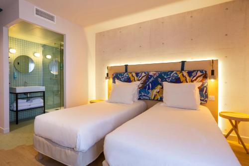two beds in a room with a bathroom at Urban Hotel & Spa Aix-les-Bains - BW Signature Collection in Aix-les-Bains