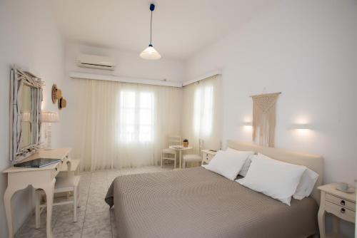 a white bedroom with a bed and a desk at Hotel Charissi in Mikonos