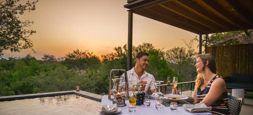 a man and woman sitting at a table by a pool at Lion Sands Ivory Lodge in Sabi Sand Game Reserve
