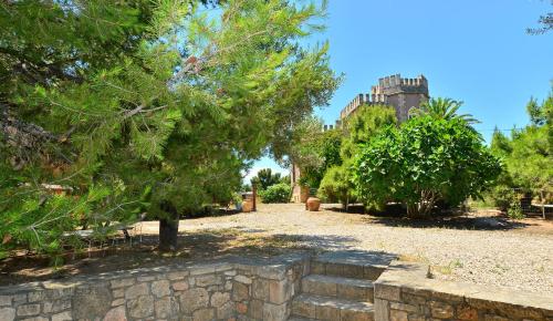 a garden with a stone wall and trees and a castle at PYRGOS RALLI ESTATE Guesthouse in Aegina Town