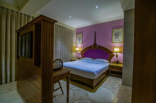 a bedroom with a bed with purple walls and a desk at Hotel Sai Palace , Mangalore in Mangalore