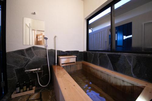 a bathroom with a tub filled with water and a window at Oyado Den Rikyu in Yufuin