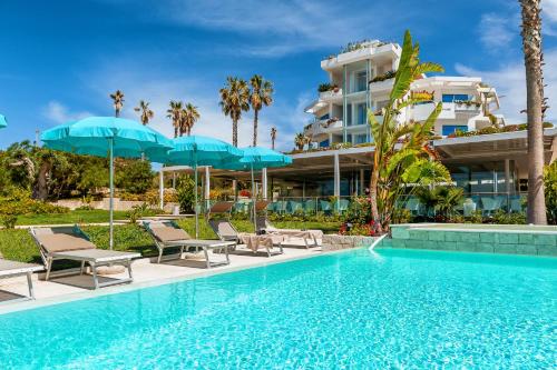 a pool with chairs and umbrellas next to a building at Acacia Palace in Marina di Ragusa