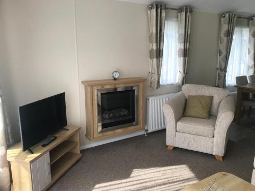 a living room with a fireplace and a chair and a television at Poppy at Oakdene Forest Park in Ringwood
