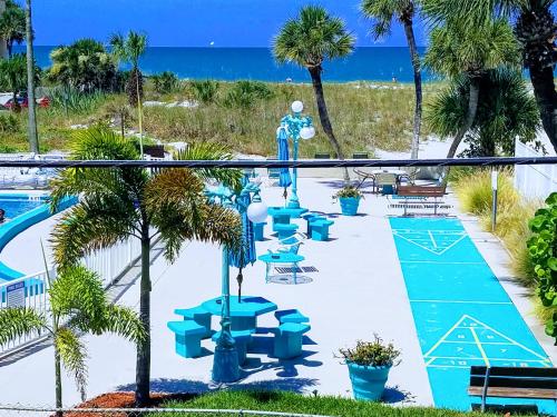 uma piscina com mesas e cadeiras azuis e o oceano em Johns Pass Beach Motel em St. Pete Beach