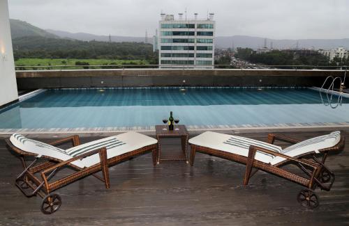 Country Inn & Suites By Radisson Navi Mumbai في نافي مومباي: مسبح مع كرسيين وطاولة على مبنى