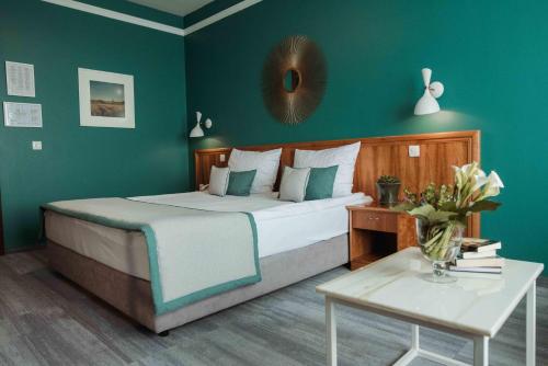 Un dormitorio con una cama con paredes verdes y una mesa. en Hotel Đakovo, en Ðakovo