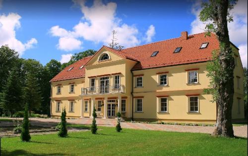 une grande maison jaune avec un toit rouge dans l'établissement Ziemupes Muiža & SPA, à Ziemupe