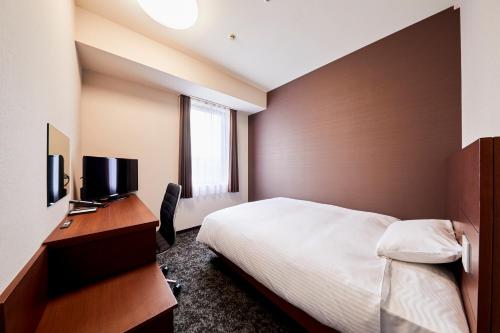 a bedroom with a bed and a desk with a television at Hotel Wing International Kobe - Shinnagata Ekimae in Kobe