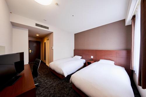 a hotel room with two beds and a flat screen tv at Hotel Wing International Kobe - Shinnagata Ekimae in Kobe