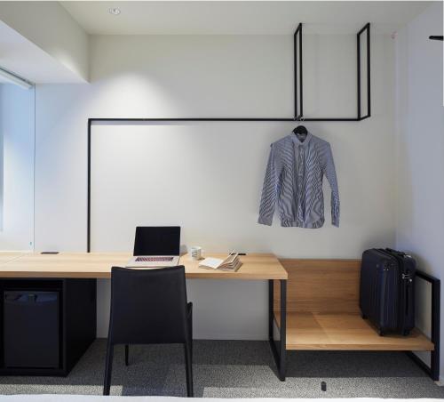 a desk with a laptop and a jacket hanging on a wall at hotel androoms Nagoya Fushimi in Nagoya