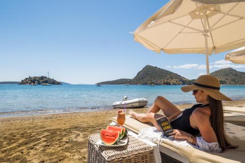 a woman sitting on a beach under an umbrella at Nelly's Apartments in Tolo