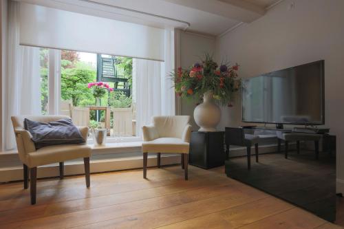 een woonkamer met een televisie, stoelen en een tafel bij EMPIRIC Keizersgracht in Amsterdam