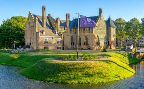 a large building with a flag in front of a river at Het Ankertje (Oosterhaven) in Medemblik
