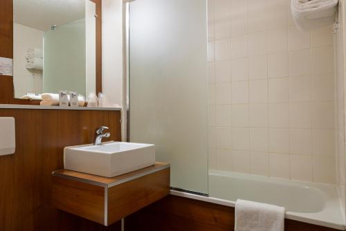 a bathroom with a tub, sink, and shower at Comfort Hotel Aeroport Lyon St Exupery in Saint-Exupéry