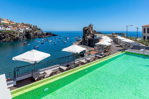 a swimming pool with umbrellas and boats in the water at Pestana Churchill Bay in Câmara de Lobos