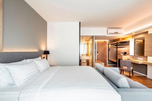 a bedroom with a large white bed and a kitchen at Hotel Amber Pattaya in Pattaya Central