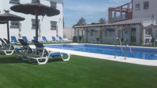 una piscina con sillas y sombrillas junto a un edificio en Hotel Cortijo Los Gallos, en Chiclana de la Frontera