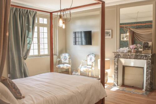 a bedroom with a bed and a fireplace with two chairs at Le manoir des chevaux dorés in Le Neubourg