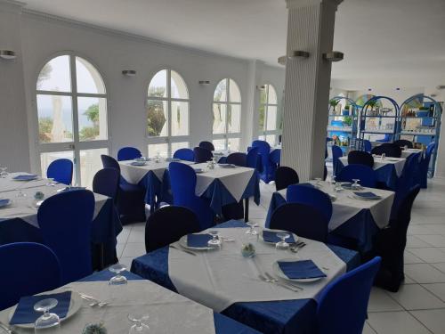 una sala da pranzo con tavoli, sedie blu e finestre di Hotel Caraibisiaco sul mare a San Pietro in Bevagna