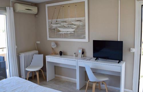 Schlafzimmer mit einem Schreibtisch, einem TV und Stühlen in der Unterkunft Hotel L'Orangeraie in Le Lavandou