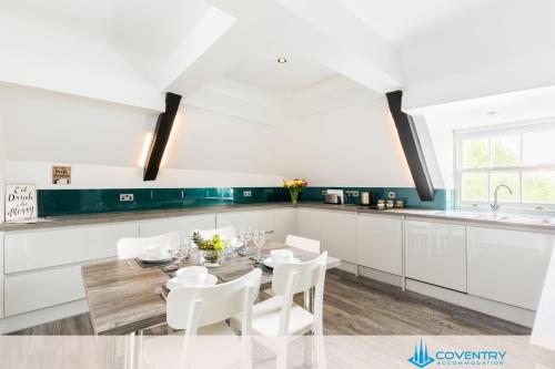 a white kitchen with a table and white chairs at 2 Bedroom Apartment, NEC, HS2, BHX, JLR - Devereux House, Hosted By Coventry Accommodation in Coleshill