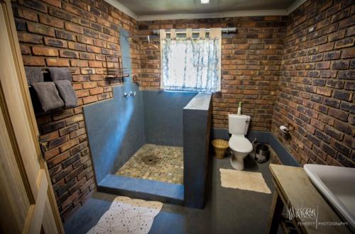 a bathroom with a tub and a toilet and a brick wall at Rio Dos Elefantes River Camp in Hoedspruit