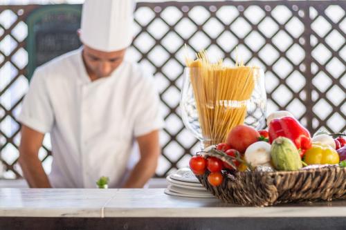 a chef standing next to a basket of fruits and vegetables at Lardos Bay Hotel in Lardos