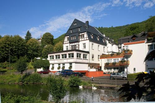 a large white building with a black roof next to a river at Bertricher Hof Hotel Garni in Bad Bertrich