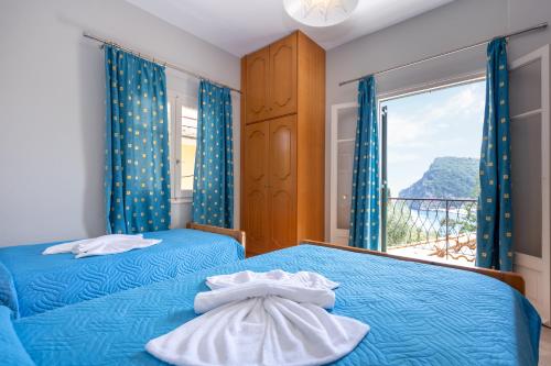 a bedroom with two beds with blue sheets and a window at Rapanos Apartments in Paleokastritsa