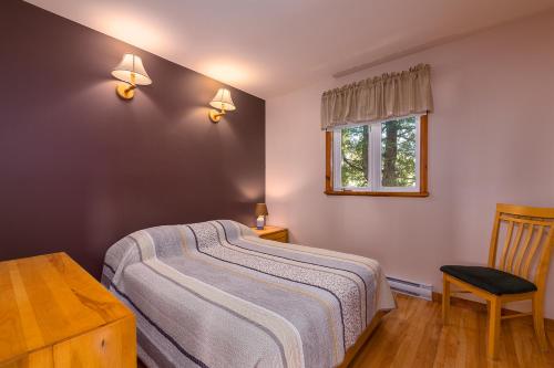 a bedroom with a bed and a chair and a window at Domaine Frais Air in La Malbaie