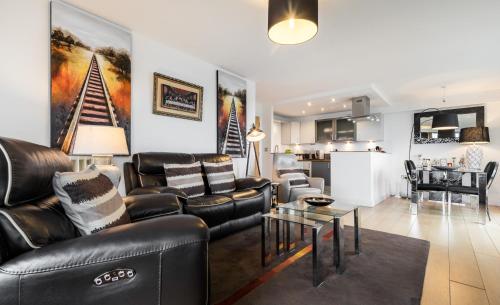 a living room with black leather furniture and a kitchen at COSY RIVERVIEW-LONDON EXCEL CENTRE-O2 ARENA in London