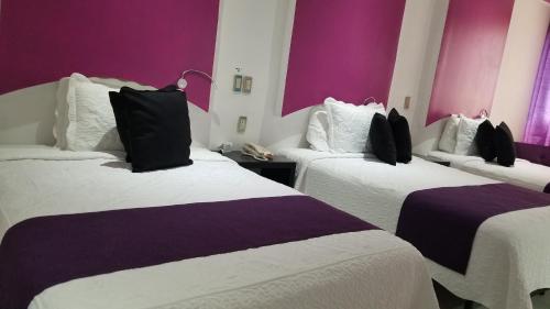 Habitación de hotel con 2 camas y paredes moradas en Hotel Dluxe, en San Juan de los Lagos