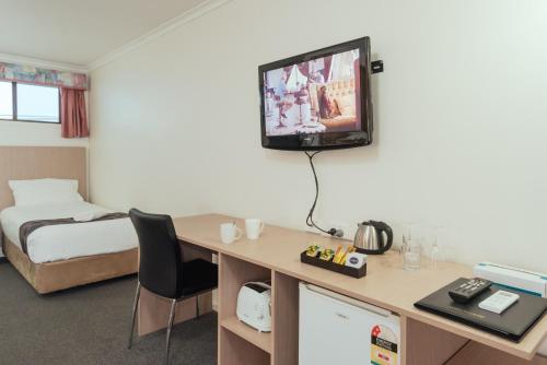 a hotel room with a desk and a tv on the wall at Coffs Windmill Motel in Coffs Harbour